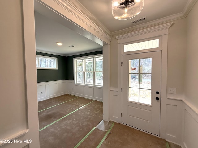 doorway to outside with ornamental molding, a wainscoted wall, visible vents, and a decorative wall