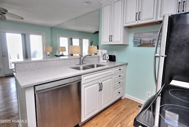 kitchen with appliances with stainless steel finishes, sink, white cabinets, kitchen peninsula, and light wood-type flooring