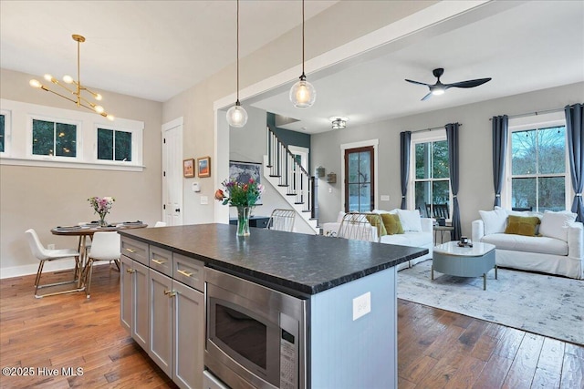 kitchen featuring dark countertops, dark wood finished floors, stainless steel microwave, decorative light fixtures, and open floor plan