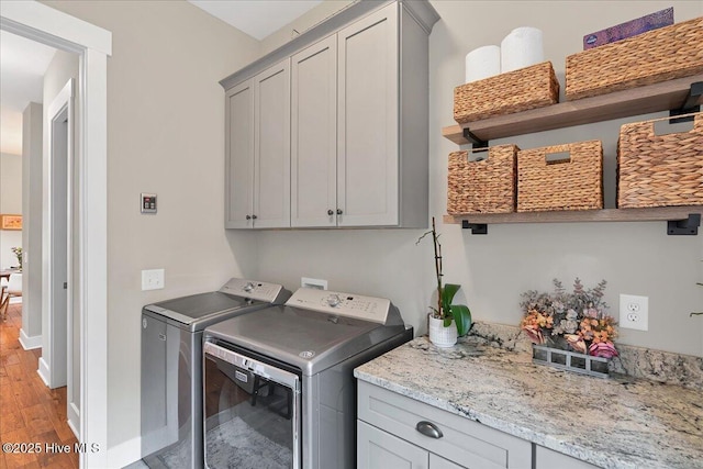 laundry area featuring baseboards, cabinet space, light wood-style floors, and washer and clothes dryer