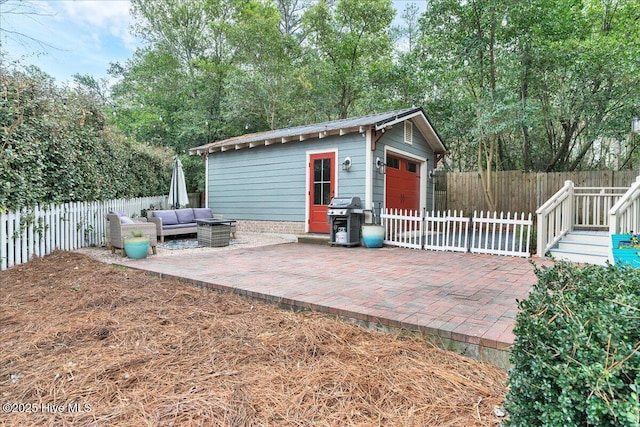 view of patio with grilling area, a detached garage, fence private yard, outdoor lounge area, and an outbuilding