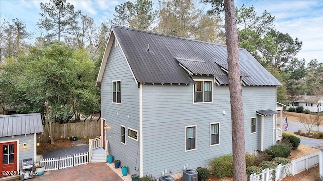 back of property featuring metal roof, central AC unit, and fence