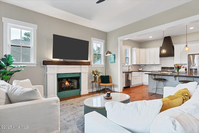 living room with recessed lighting, plenty of natural light, a warm lit fireplace, and wood finished floors