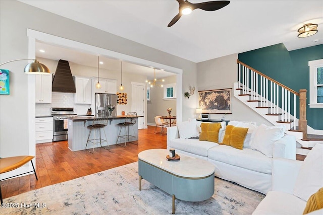 living area with stairway, light wood-style flooring, and ceiling fan