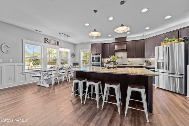 kitchen with light stone counters, decorative light fixtures, dark brown cabinets, a kitchen island, and stainless steel appliances