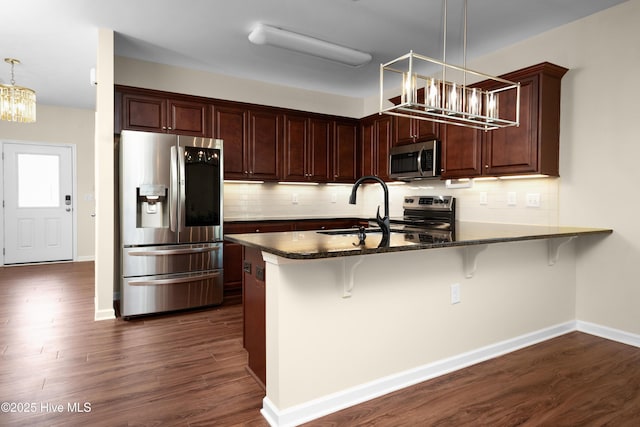 kitchen featuring a sink, a chandelier, stainless steel appliances, a peninsula, and tasteful backsplash