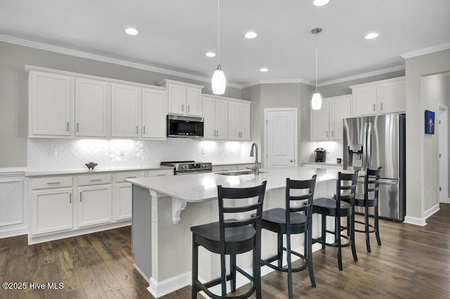 kitchen featuring sink, appliances with stainless steel finishes, white cabinetry, hanging light fixtures, and an island with sink