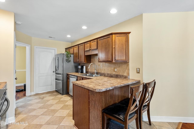 kitchen with a breakfast bar area, tasteful backsplash, appliances with stainless steel finishes, a sink, and a peninsula