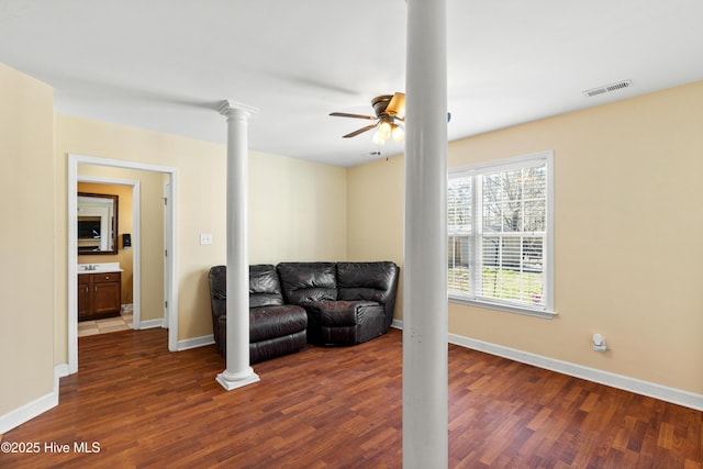 living room featuring dark wood-type flooring, a ceiling fan, baseboards, visible vents, and ornate columns