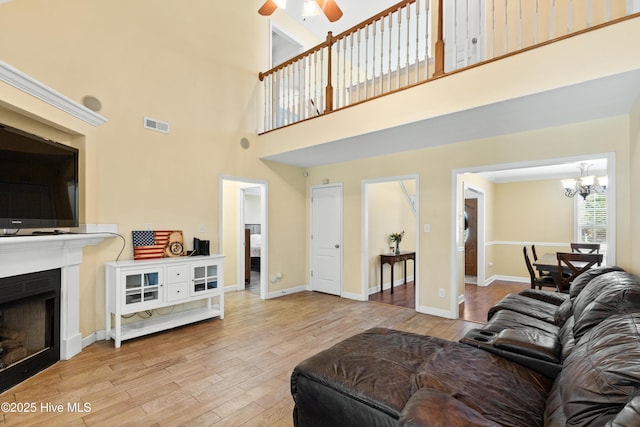 living area featuring baseboards, visible vents, wood finished floors, a fireplace, and ceiling fan with notable chandelier