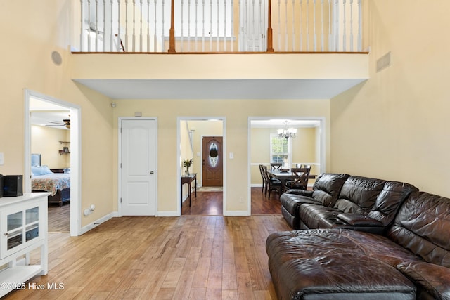 living area featuring visible vents, baseboards, a towering ceiling, light wood-type flooring, and a notable chandelier