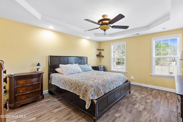 bedroom with a tray ceiling, multiple windows, baseboards, and wood finished floors