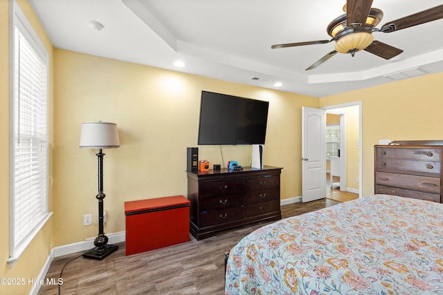 bedroom featuring visible vents, multiple windows, a tray ceiling, and baseboards