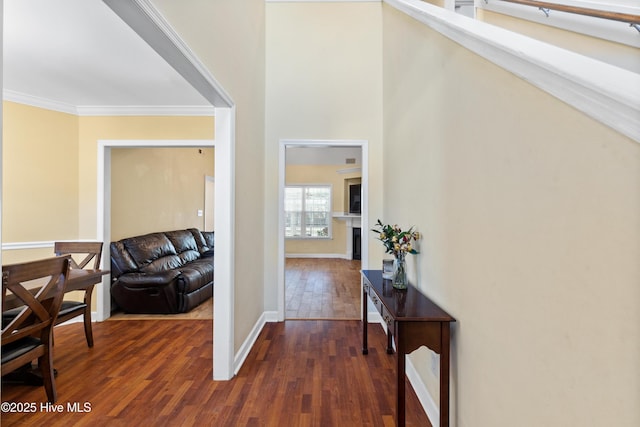 hallway with ornamental molding, dark wood finished floors, a towering ceiling, and baseboards