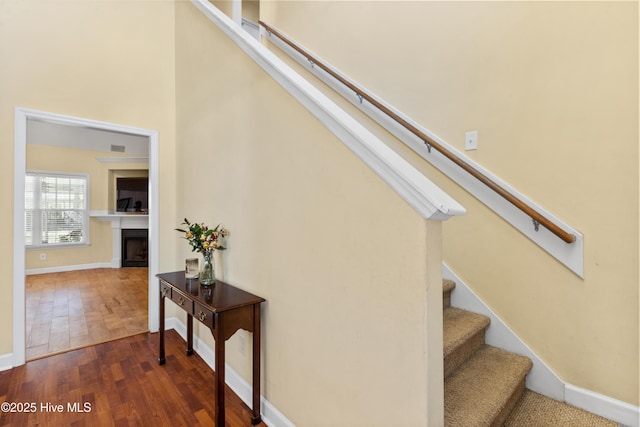 stairway with a fireplace, a towering ceiling, baseboards, and wood finished floors