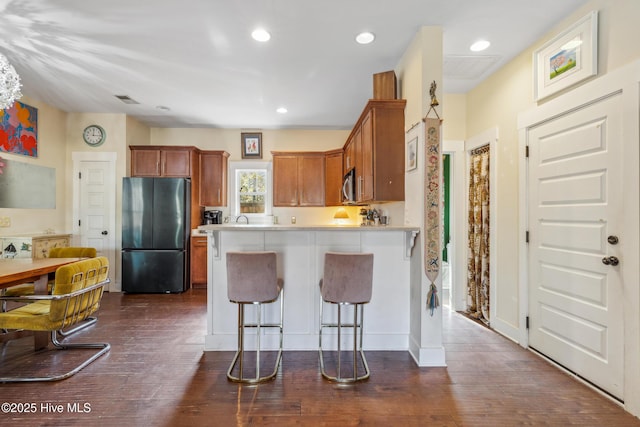 kitchen with black refrigerator, a kitchen breakfast bar, kitchen peninsula, and dark wood-type flooring