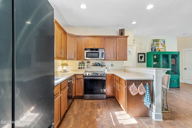 kitchen with hardwood / wood-style flooring, a breakfast bar, kitchen peninsula, and appliances with stainless steel finishes