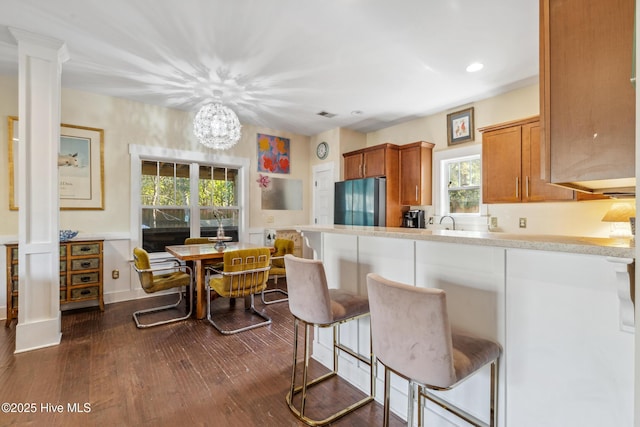 kitchen featuring sink, dark hardwood / wood-style flooring, stainless steel fridge, a kitchen breakfast bar, and decorative columns