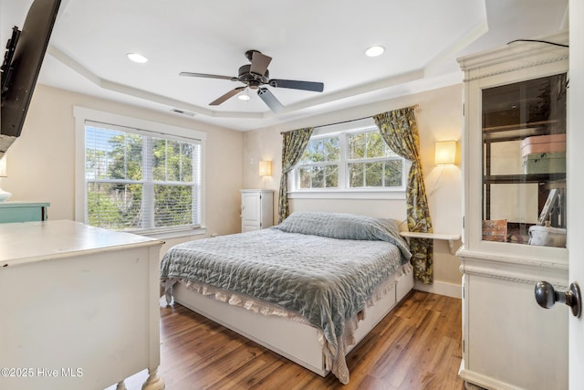 bedroom featuring ceiling fan, a tray ceiling, hardwood / wood-style floors, and multiple windows