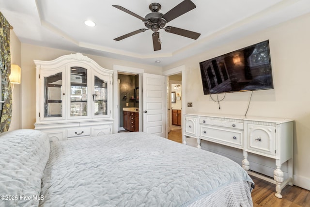 bedroom featuring dark hardwood / wood-style floors, a raised ceiling, ceiling fan, and ensuite bathroom