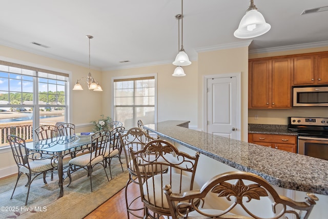 kitchen with crown molding, hanging light fixtures, dark stone countertops, stainless steel appliances, and light hardwood / wood-style floors