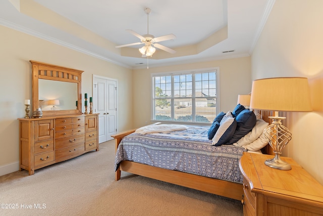 carpeted bedroom featuring ceiling fan, ornamental molding, a tray ceiling, and a closet