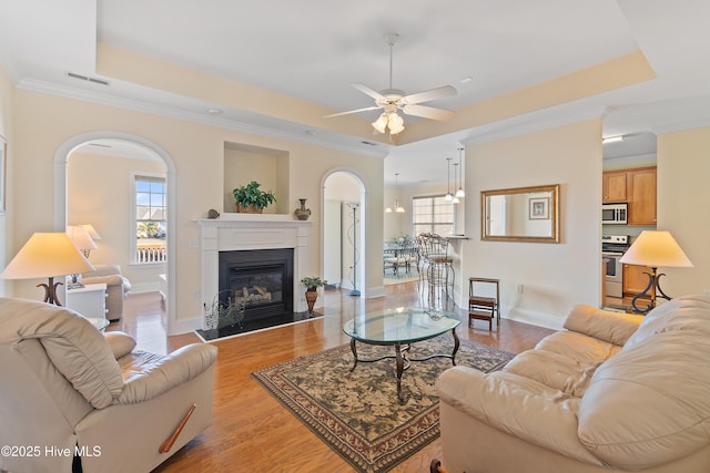 living room with crown molding, plenty of natural light, a tray ceiling, and light hardwood / wood-style floors