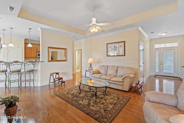 living room with crown molding, ceiling fan, a tray ceiling, and light hardwood / wood-style floors