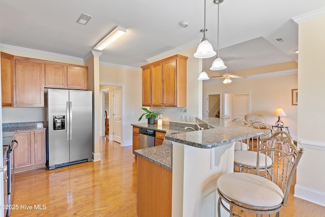 kitchen with appliances with stainless steel finishes, a kitchen bar, ornamental molding, kitchen peninsula, and light wood-type flooring