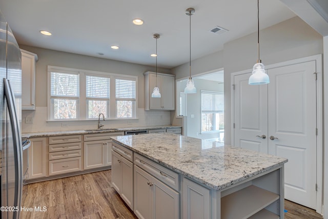 kitchen with pendant lighting, sink, stainless steel fridge, light hardwood / wood-style flooring, and a kitchen island