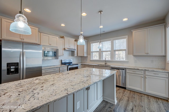 kitchen featuring stainless steel appliances, sink, pendant lighting, and light stone counters