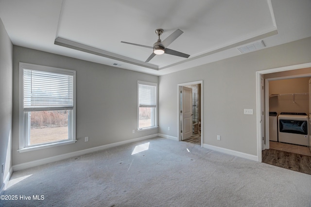 unfurnished bedroom featuring ensuite bathroom, washer and dryer, light carpet, a walk in closet, and a raised ceiling