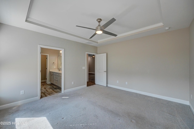 unfurnished bedroom featuring ceiling fan, light carpet, ensuite bath, and a tray ceiling