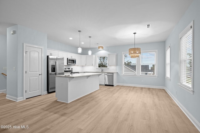 kitchen featuring decorative light fixtures, a center island, light hardwood / wood-style flooring, stainless steel appliances, and white cabinets