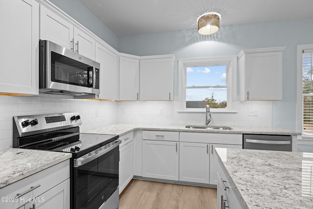 kitchen featuring sink, white cabinetry, light wood-type flooring, stainless steel appliances, and light stone countertops