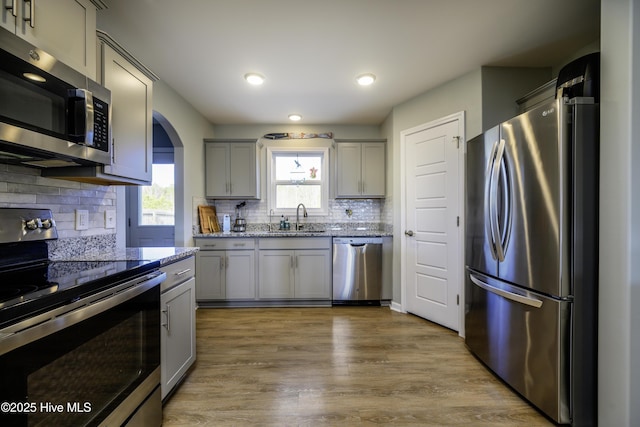 kitchen with appliances with stainless steel finishes, sink, gray cabinetry, hardwood / wood-style flooring, and light stone countertops