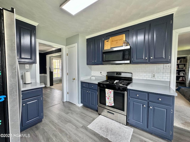 kitchen featuring tasteful backsplash, light wood-type flooring, blue cabinets, and appliances with stainless steel finishes