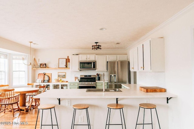 kitchen with appliances with stainless steel finishes, sink, white cabinets, and a kitchen bar