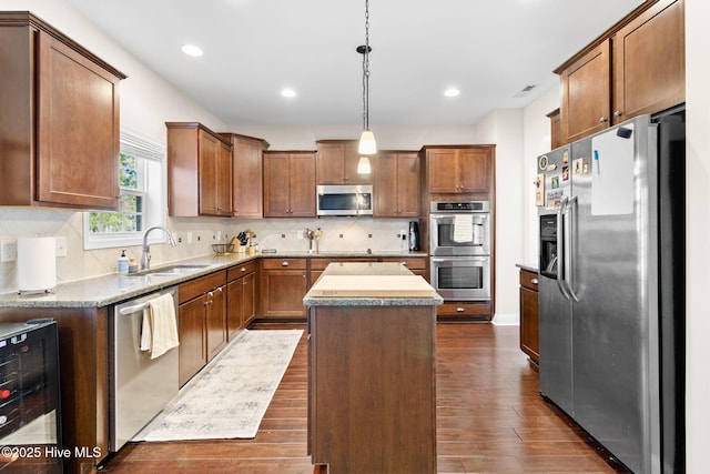 kitchen featuring sink, a center island, pendant lighting, stainless steel appliances, and beverage cooler