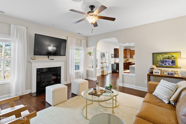 living room with a wealth of natural light, decorative columns, dark hardwood / wood-style floors, and ceiling fan