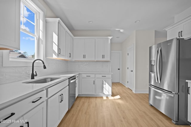 kitchen with appliances with stainless steel finishes, white cabinetry, sink, backsplash, and light wood-type flooring