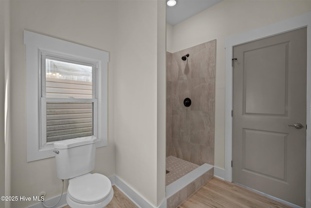 bathroom featuring wood-type flooring, toilet, and a tile shower