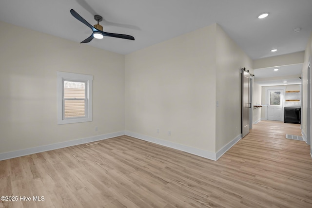 spare room featuring a barn door, ceiling fan, and light hardwood / wood-style flooring