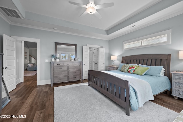 bedroom featuring dark wood-type flooring, ceiling fan, a tray ceiling, and multiple windows