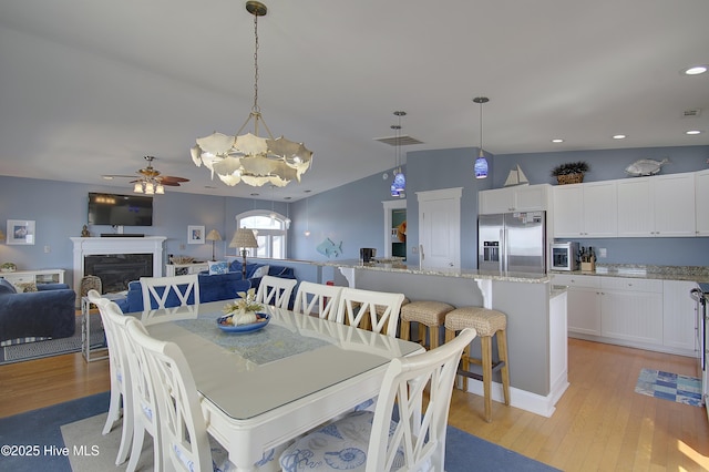 dining area featuring vaulted ceiling, a high end fireplace, ceiling fan, and light hardwood / wood-style floors