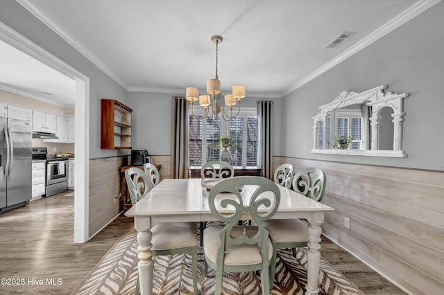 dining room featuring wood walls, light wood-type flooring, an inviting chandelier, and ornamental molding