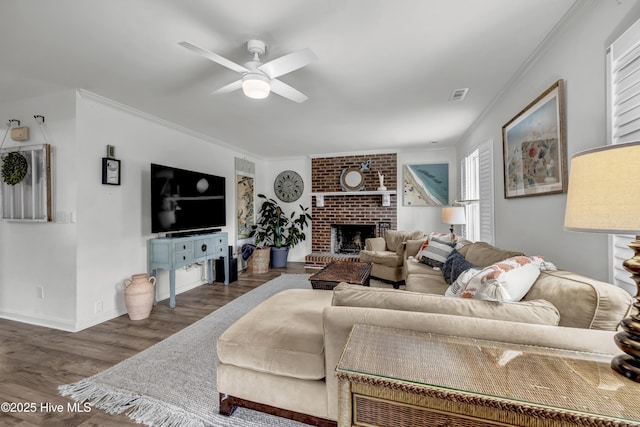 living room with ceiling fan, a brick fireplace, crown molding, and dark wood-type flooring