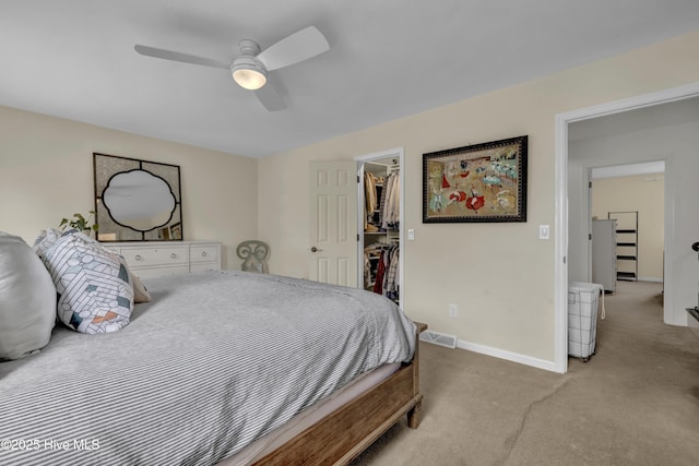 bedroom with a walk in closet, light colored carpet, and ceiling fan