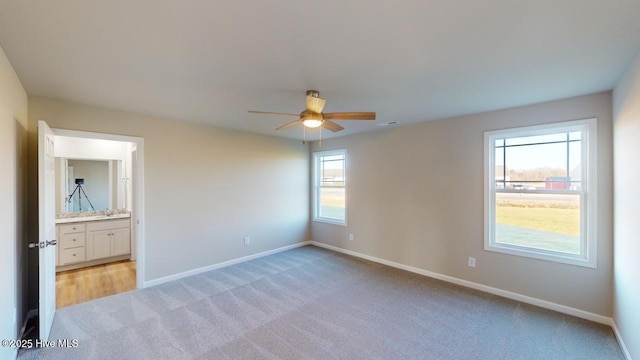 unfurnished bedroom with ceiling fan, light colored carpet, and ensuite bathroom