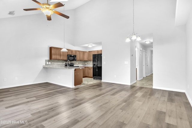 kitchen featuring pendant lighting, kitchen peninsula, backsplash, black appliances, and light hardwood / wood-style flooring